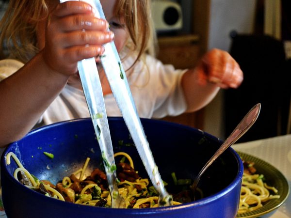 Ett litet barn tar pasta och grönsaker ur en stor skål.
