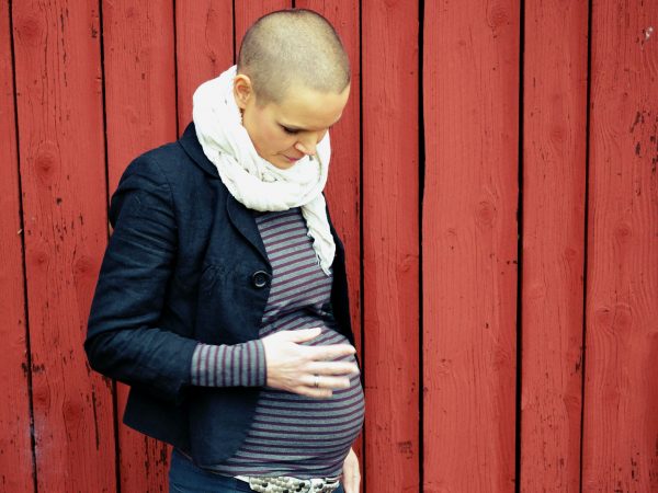Jag står med en faluröd vägg som bakgrund och håller en hand på min gravida mage