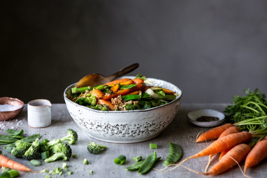 Stekt ris i en skål med massor av krispiga grönsaker. Morötter och broccoli ligger runt om.