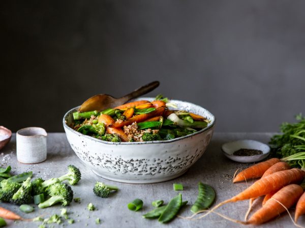 Stekt ris i en skål med massor av krispiga grönsaker. Morötter och broccoli ligger runt om.