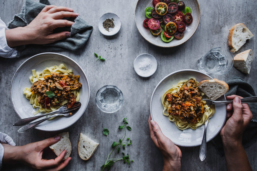 Ett bord sett uppifrån med två tallrikar pasta med köttfärssås, underbara tomater i olika färger och händer som tar för sig.