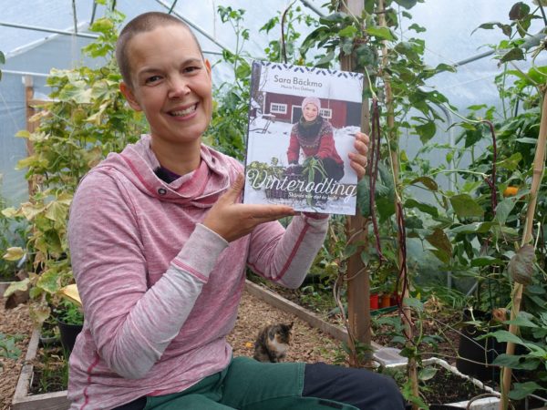 Sara Bäckmo sitter i växthuset och håller den nya boken bredvid sig.