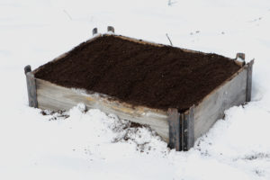 En pallkrage mitt i snön full med jord.