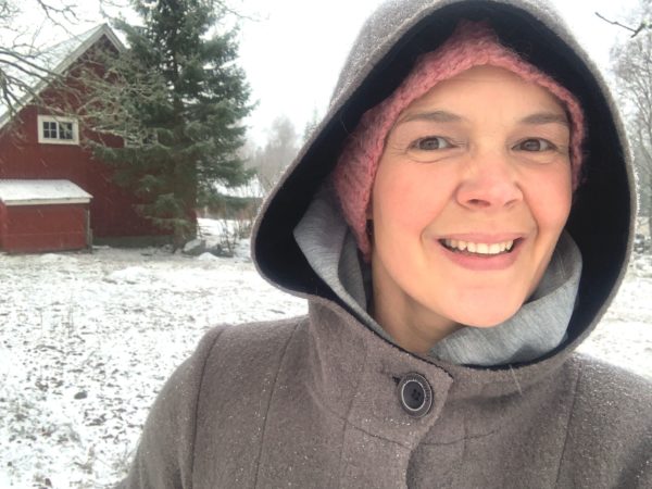 Sara Bäckmo fotograferad ute i ett snöigt landskap, i kappa med luva över huvudet.