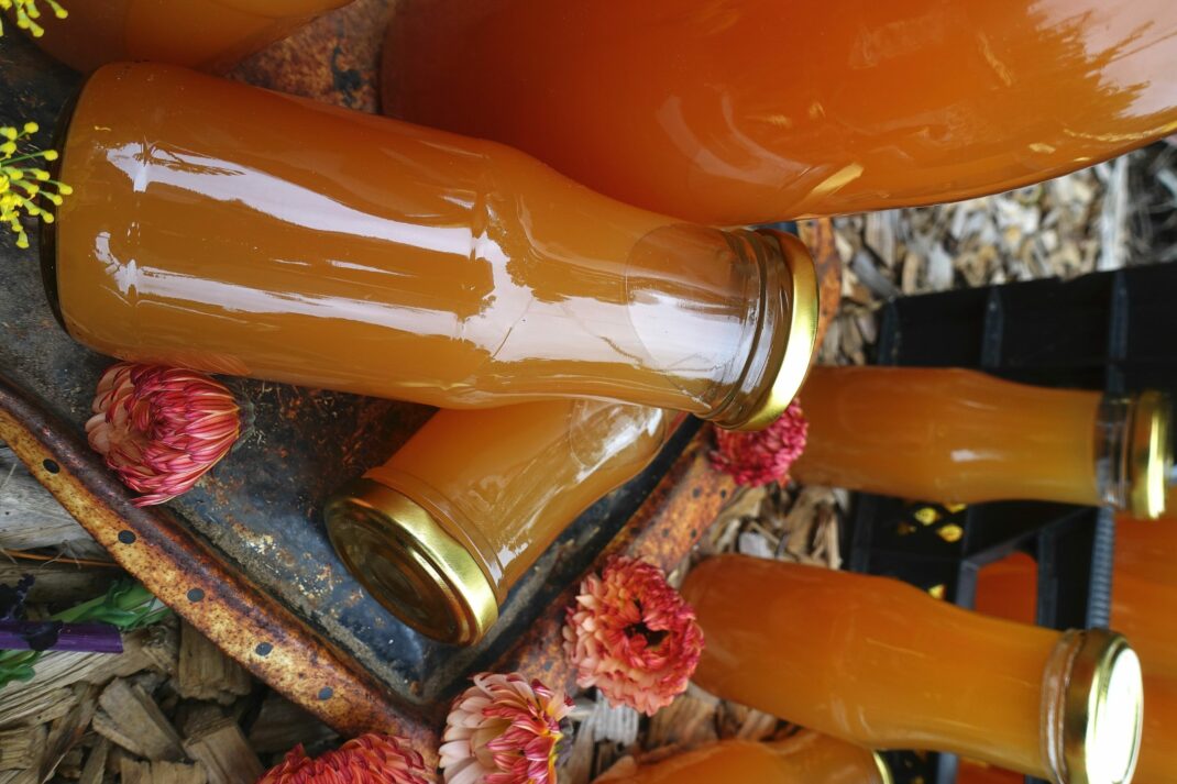 Små och stora flaskor med varmt orange must ligger och står på träflis utomhus.