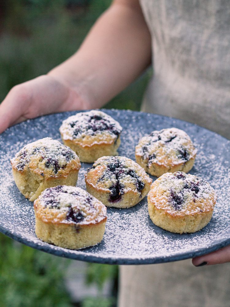 Nybakta blåbärsmuffins pudrade med florsocker serverade på ett blått fat.