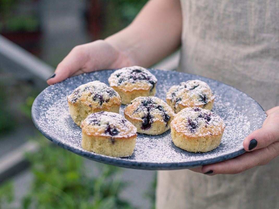 Nybakta blåbärsmuffins pudrade med florsocker serverade på ett blått fat.