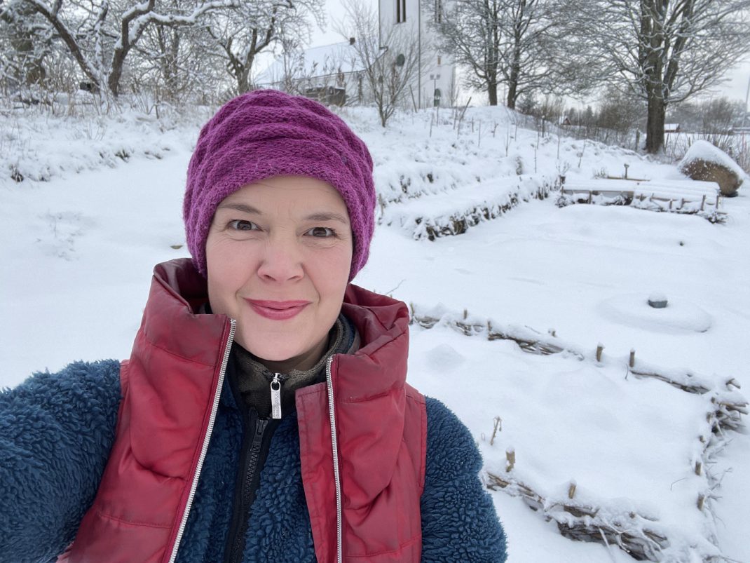 En glad Sara Bäckmo i knalliga färger framför en snötäckt köksträdgård.