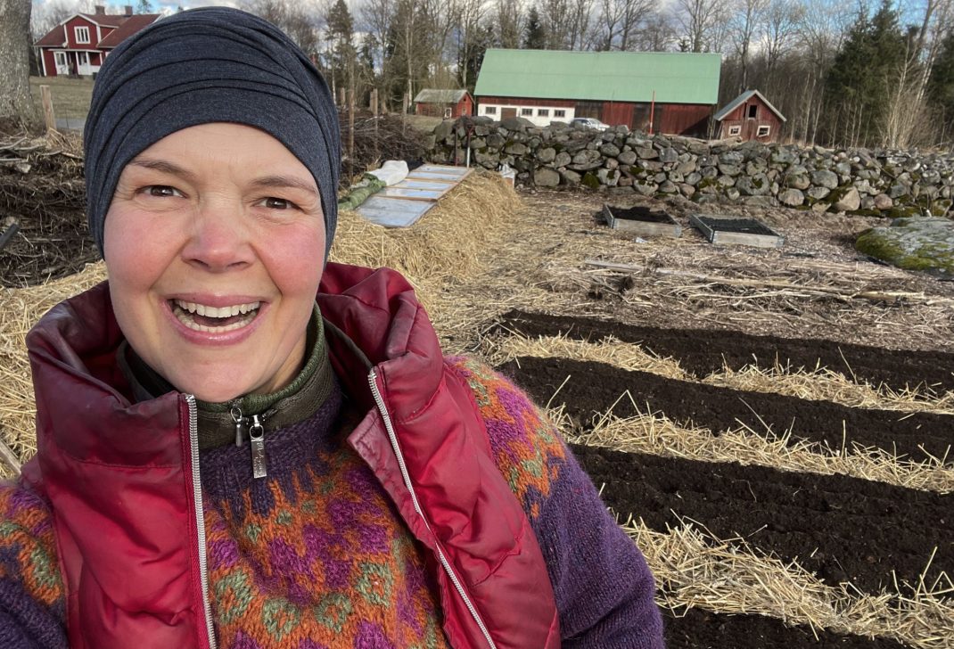 Glad Sara framför odlingsbäddar med svart jord. 